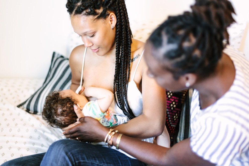Black mom breastfeeding baby while Black lactation consultant looks on