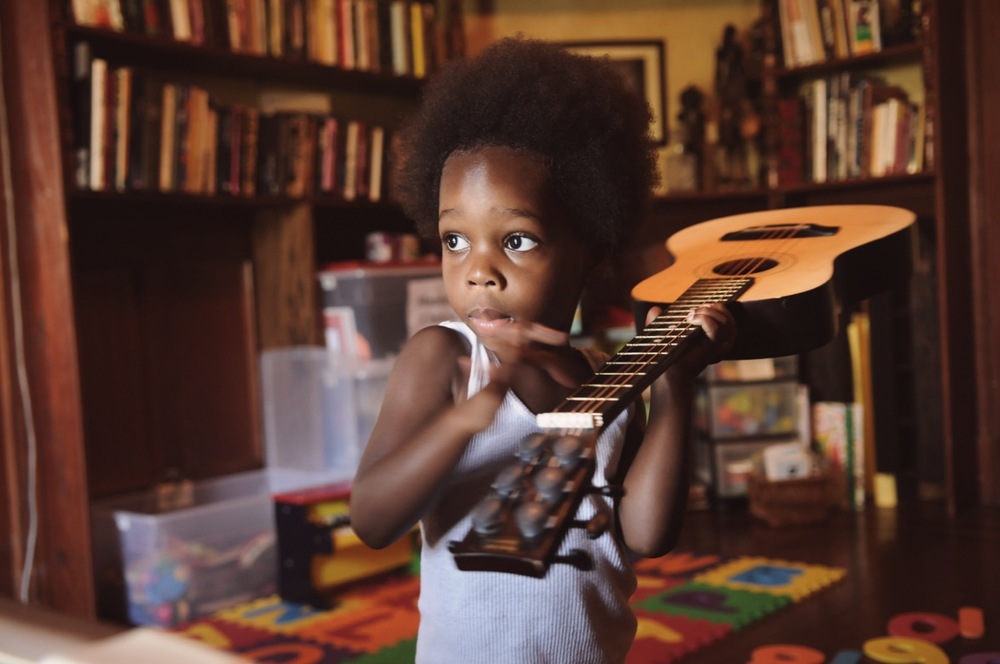 Black boy holding guitar over his shoulder black kids music article