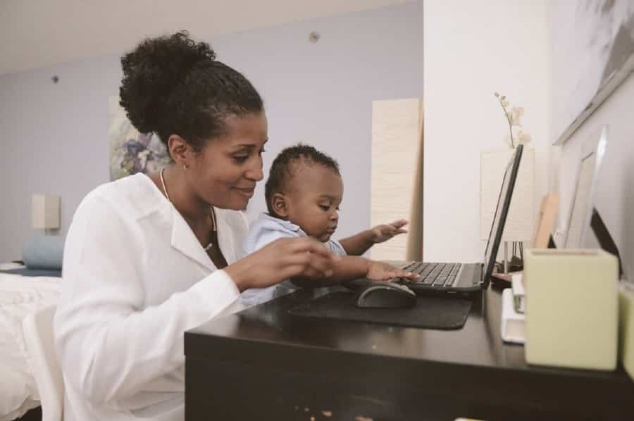Black mom working on laptop with son in lap