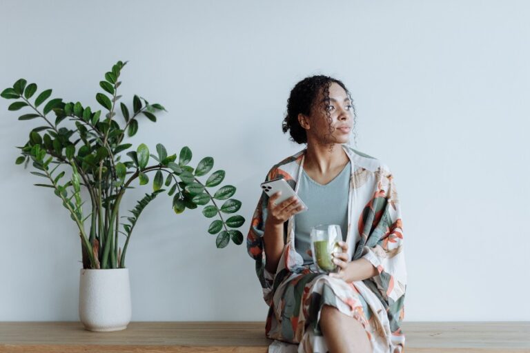 black woman thinking while holding phone and green smoothie